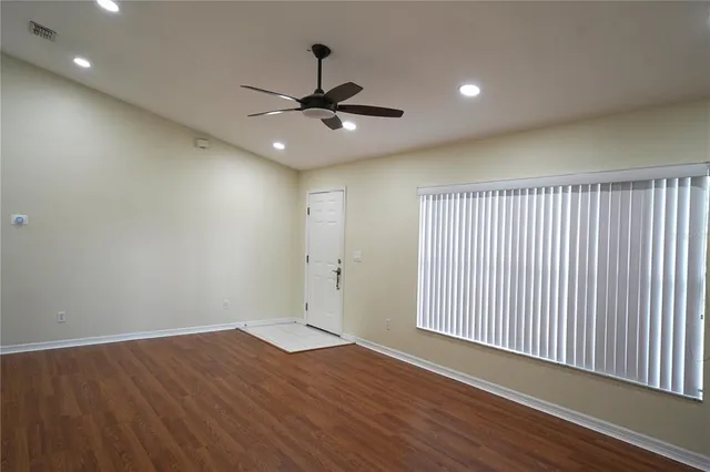 a view of an empty room with wooden floor and a ceiling fan