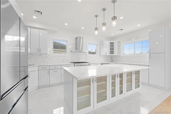 a large white kitchen with a large counter top a sink stainless steel appliances and cabinets