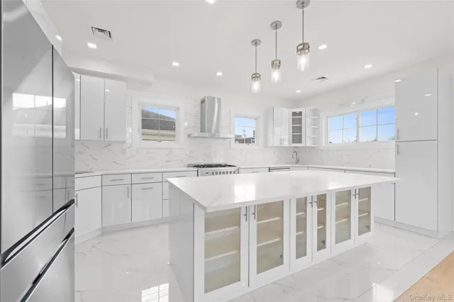 a large white kitchen with a large counter top a sink stainless steel appliances and cabinets