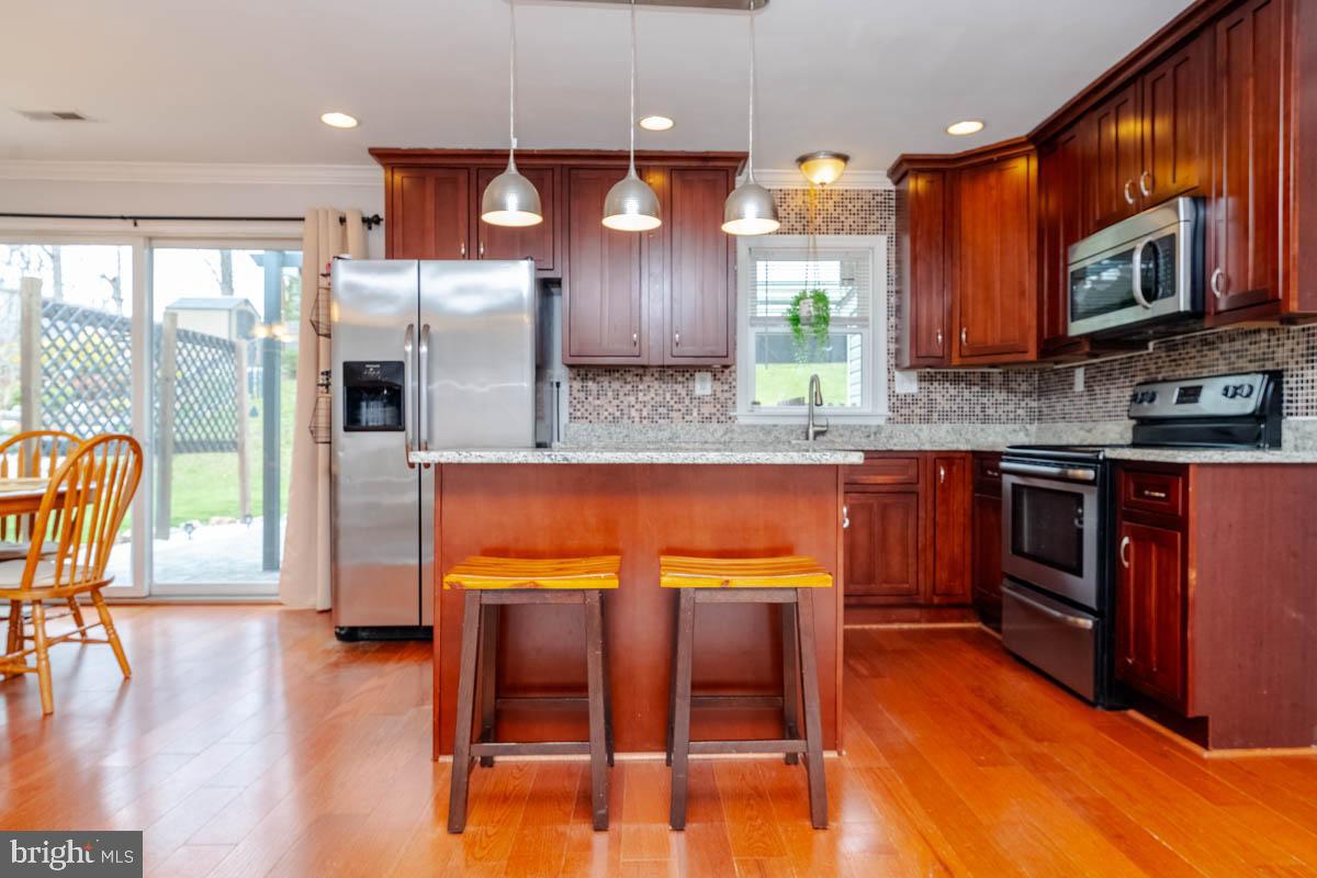 414 Enfield Road Joppa, MD 21085 - Photo 10 of 42 a kitchen with stainless steel appliances granite countertop a refrigerator a stove top oven and a dining table with wooden floor