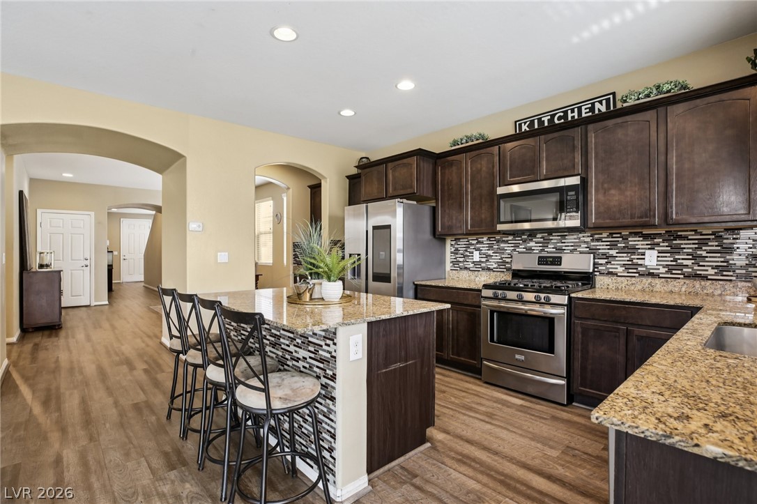3957 East Carla Ann Road North Las Vegas, NV 89081 - Photo 4 of 35 Kitchen featuring stainless steel appliances, arched walkways, dark wood finish cabinetry, light stone countertops, and a kitchen island