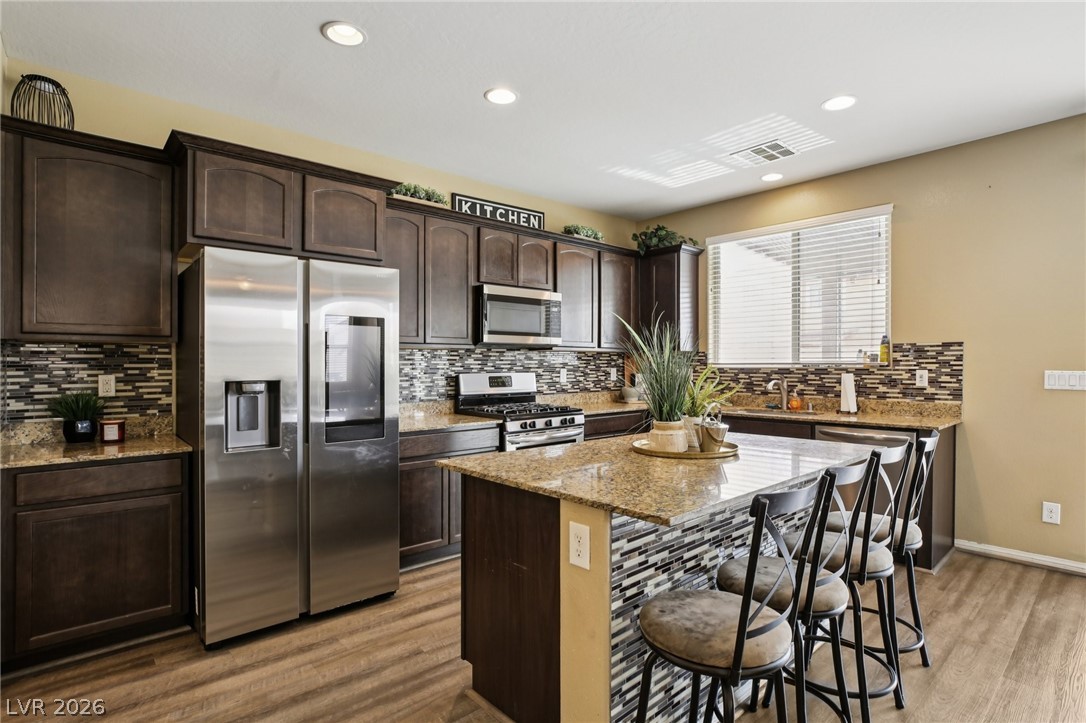 3957 East Carla Ann Road North Las Vegas, NV 89081 - Photo 5 of 35 Kitchen featuring dark wood finish cabinets, stainless steel appliances, light stone counters, light wood finished floors, and recessed lighting