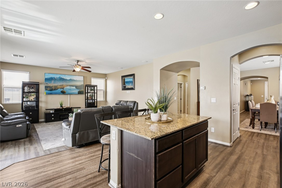 3957 East Carla Ann Road North Las Vegas, NV 89081 - Photo 32 of 35 Kitchen featuring dark wood finish cabinetry, open floor plan, light stone counters, a kitchen bar, and dark wood-style flooring
