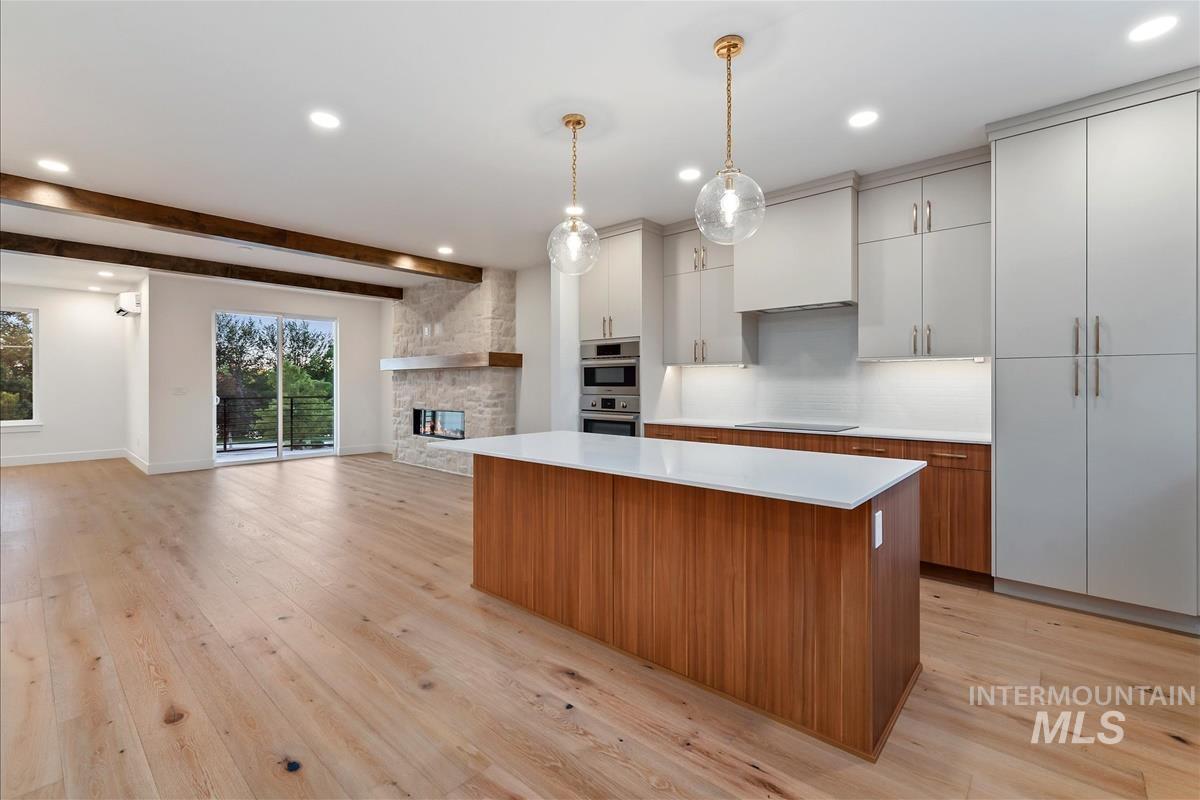 3213 West Moore Street Boise, ID 83702 - Photo 13 of 32 Open-concept living space featuring wide plank wood-finish flooring, a contemporary kitchen island with a white countertop, light-toned cabinetry, and a stone-clad fireplace with a natural wood mantel