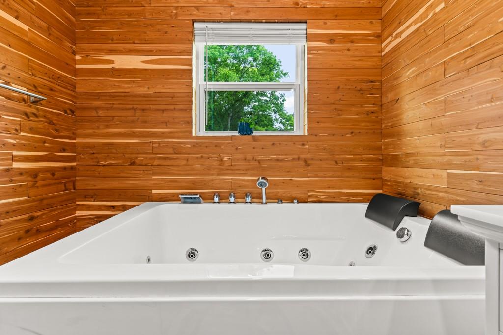 1129 Holly Road Gilmer, TX 75644 - Photo 16 of 31 Jetted soaking tub with chrome fixtures, wood-finish paneling, and an integrated window