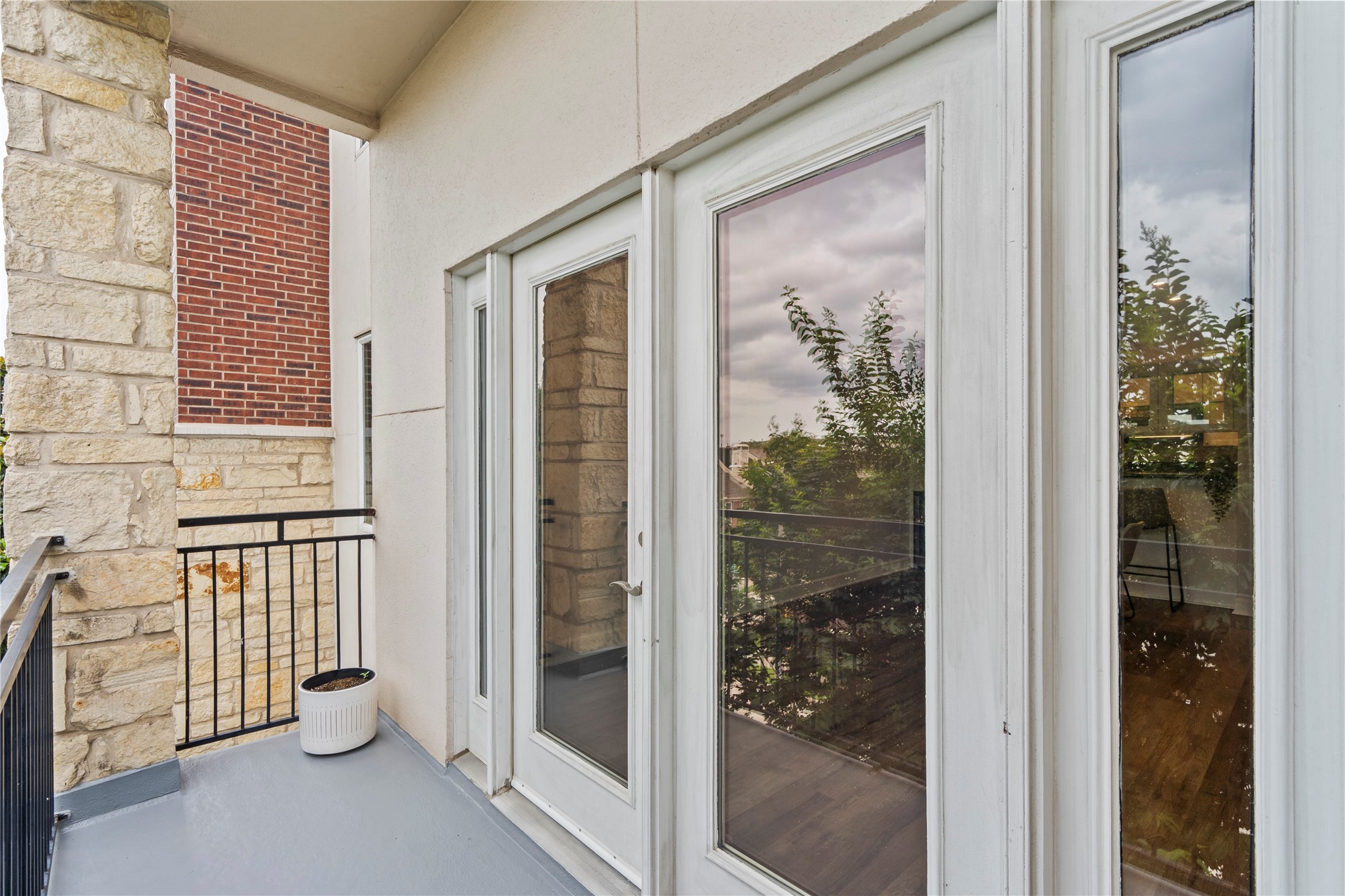 1900 Genesee Street, Unit 203 Houston, TX 77006 - Photo 24 of 30 This photo features a cozy balcony with stone and brick walls, accessed through elegant French doors. It offers a view of greenery, providing a serene outdoor space.