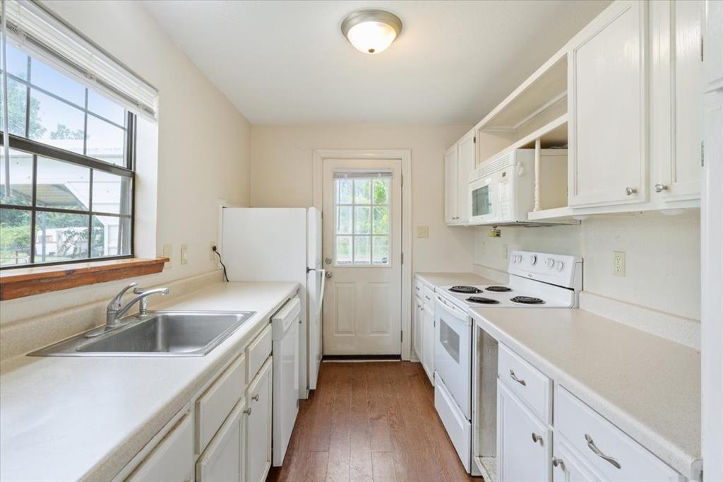 608 9th Street Hico, TX 76457 - Photo 8 of 23 Kitchen featuring white cabinetry, light-toned countertops, a stainless steel sink, wood-finish flooring, and a window with blinds