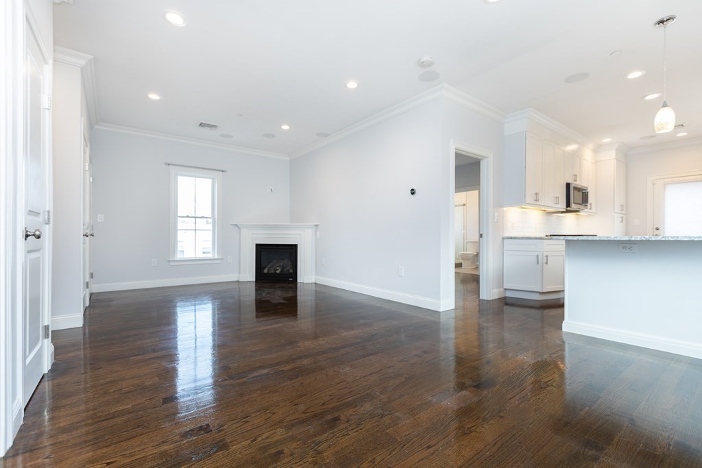 an empty room with wooden floor and a kitchen