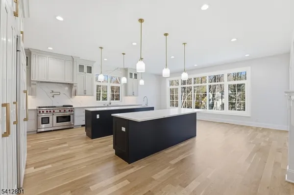 a large kitchen with stainless steel appliances granite countertop a stove a sink dishwasher a refrigerator and white cabinets with wooden floor