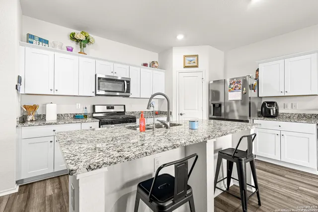 a kitchen with stainless steel appliances granite countertop a stove top oven a sink a dining table and chairs with wooden floor