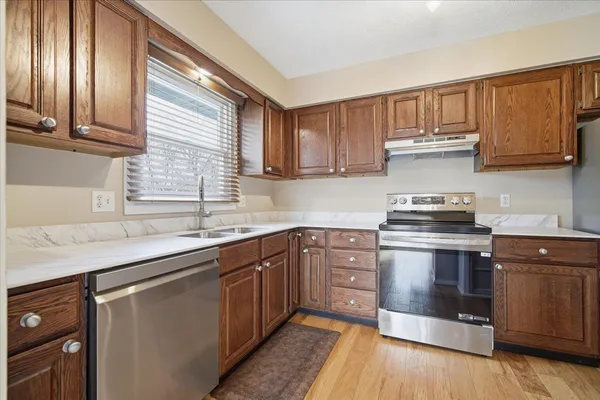a kitchen with stainless steel appliances granite countertop a refrigerator a sink a stove top oven and a dishwasher next to a window