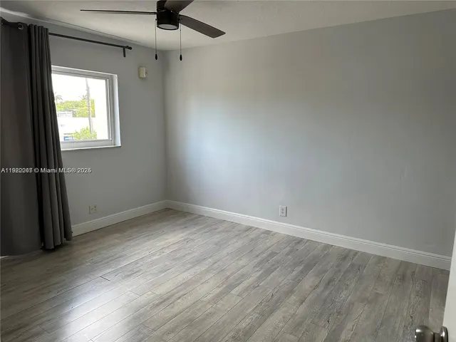 an empty room with wooden floor fan and windows