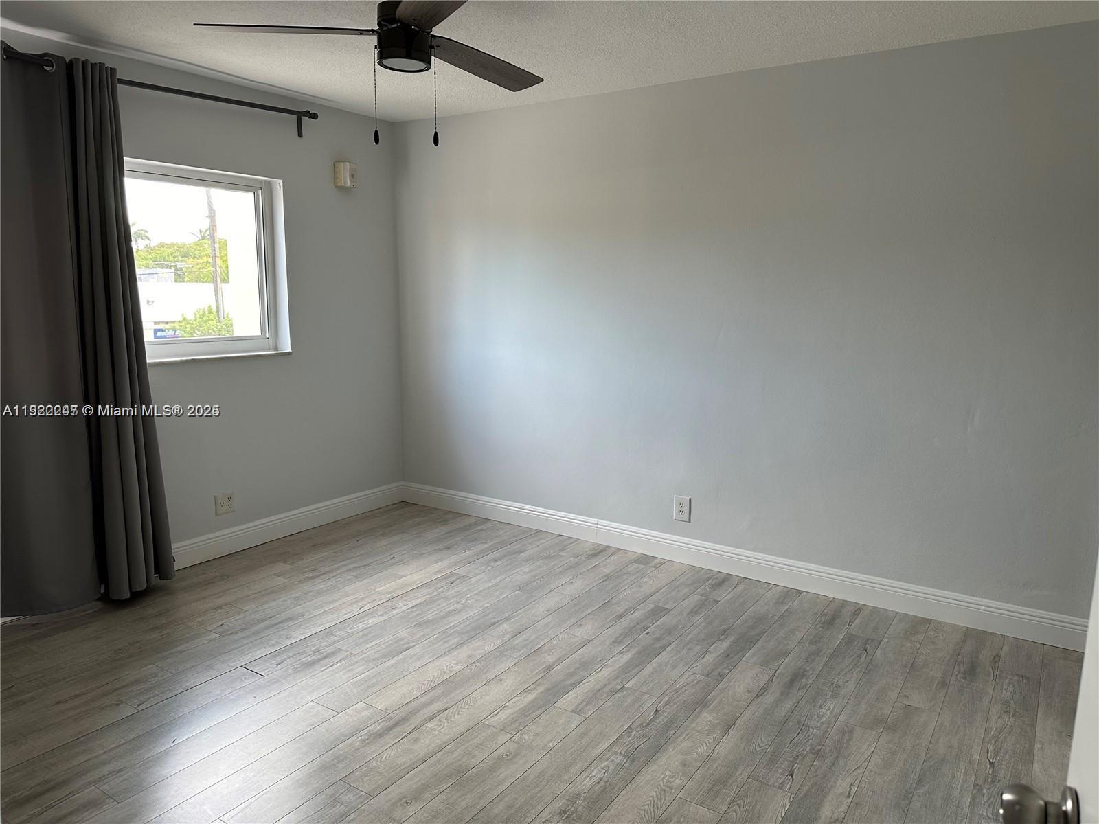 141 Northeast 10th Avenue, Unit 18B Hallandale Beach, FL 33009 - Photo 13 of 15 an empty room with wooden floor fan and windows