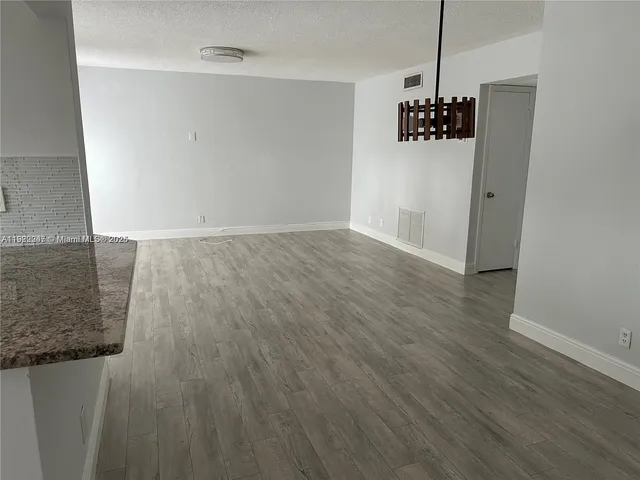 a view of a refrigerator in kitchen and an empty room with wooden floor