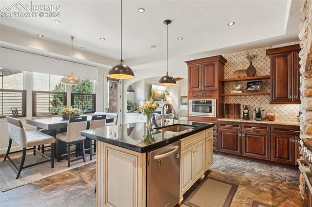 2204 Rocking Horse Court Colorado Springs, CO 80921 - Photo 7 of 50 Kitchen with appliances with stainless steel finishes, dark tile patterned floors, sink, decorative backsplash, and an island with sink