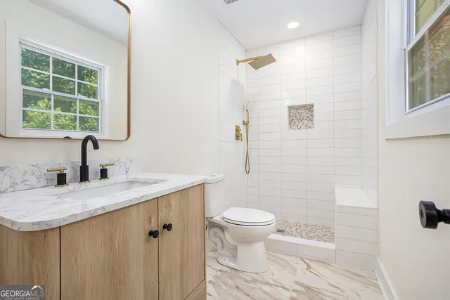 a bathroom with a granite countertop sink a toilet and a window