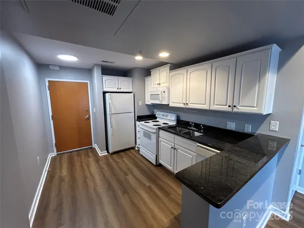 a kitchen with stainless steel appliances granite countertop a refrigerator a sink dishwasher a stove and white countertops with wooden floor