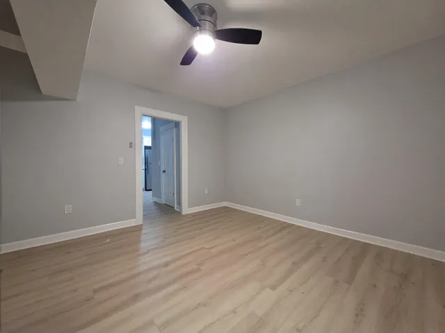 an empty room with wooden floor chandelier fan and windows