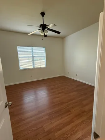 an empty room with wooden floor chandelier fan and windows