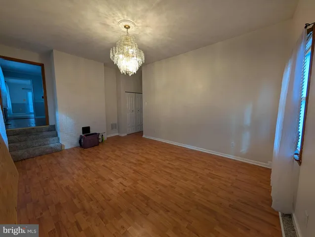 an empty room with a chandelier fan and wooden floor