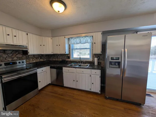 a kitchen with granite countertop stainless steel appliances a refrigerator a sink and cabinets