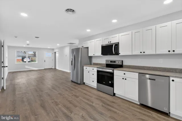 a kitchen with stainless steel appliances granite countertop a stove top oven a sink dishwasher and a refrigerator with wooden floor