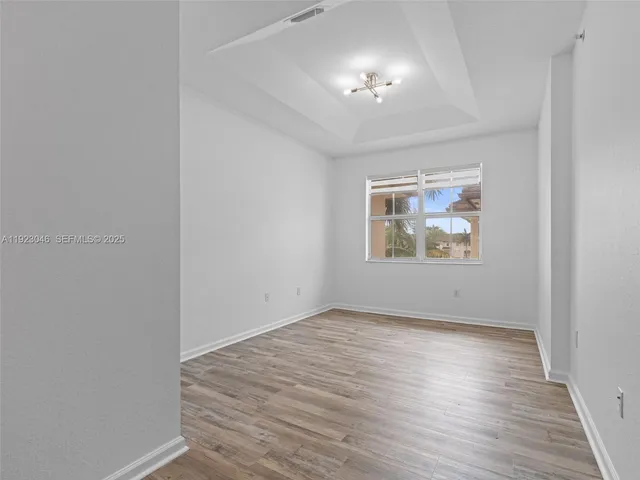 an empty room with wooden floor chandelier and windows