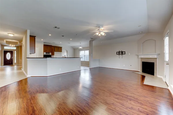 a view of a living room a kitchen with a fireplace a ceiling fan and wooden floor