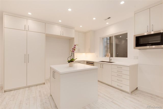 a large white kitchen with a sink dishwasher a stove and a refrigerator with wooden floor