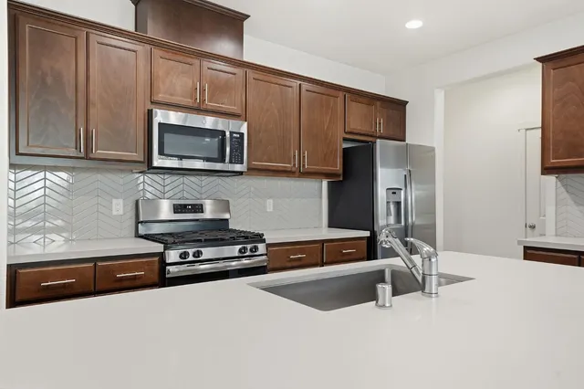 a kitchen with stainless steel appliances granite countertop a refrigerator a stove and a sink with wooden cabinets