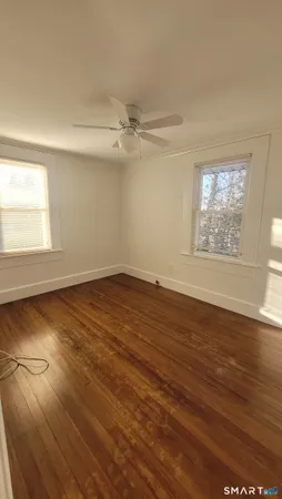 an empty room with wooden floor chandelier fan and windows