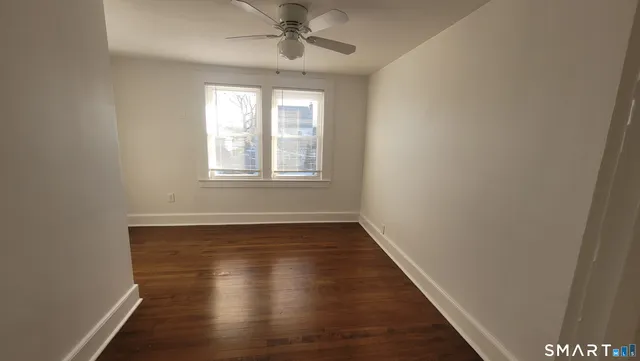 an empty room with wooden floor chandelier fan and windows