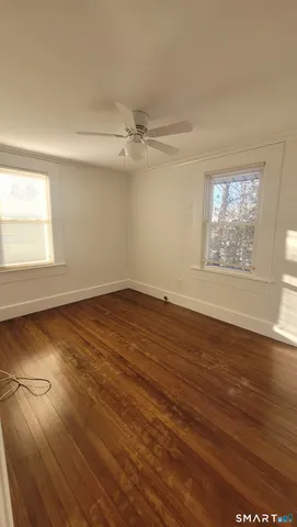 an empty room with wooden floor chandelier fan and windows