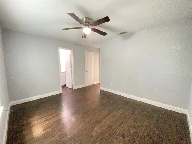 an empty room with wooden floor fan and windows