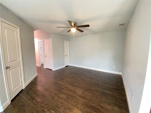 an empty room with wooden floor fan and windows