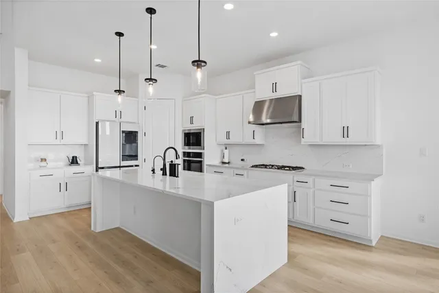 a kitchen with stainless steel appliances sink stove and white cabinets with wooden floor
