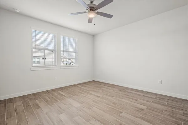 an empty room with wooden floor ceiling fan and windows