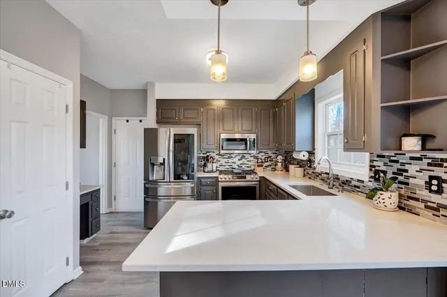 a kitchen with stainless steel appliances a stove a sink a refrigerator wooden floor and white cabinets