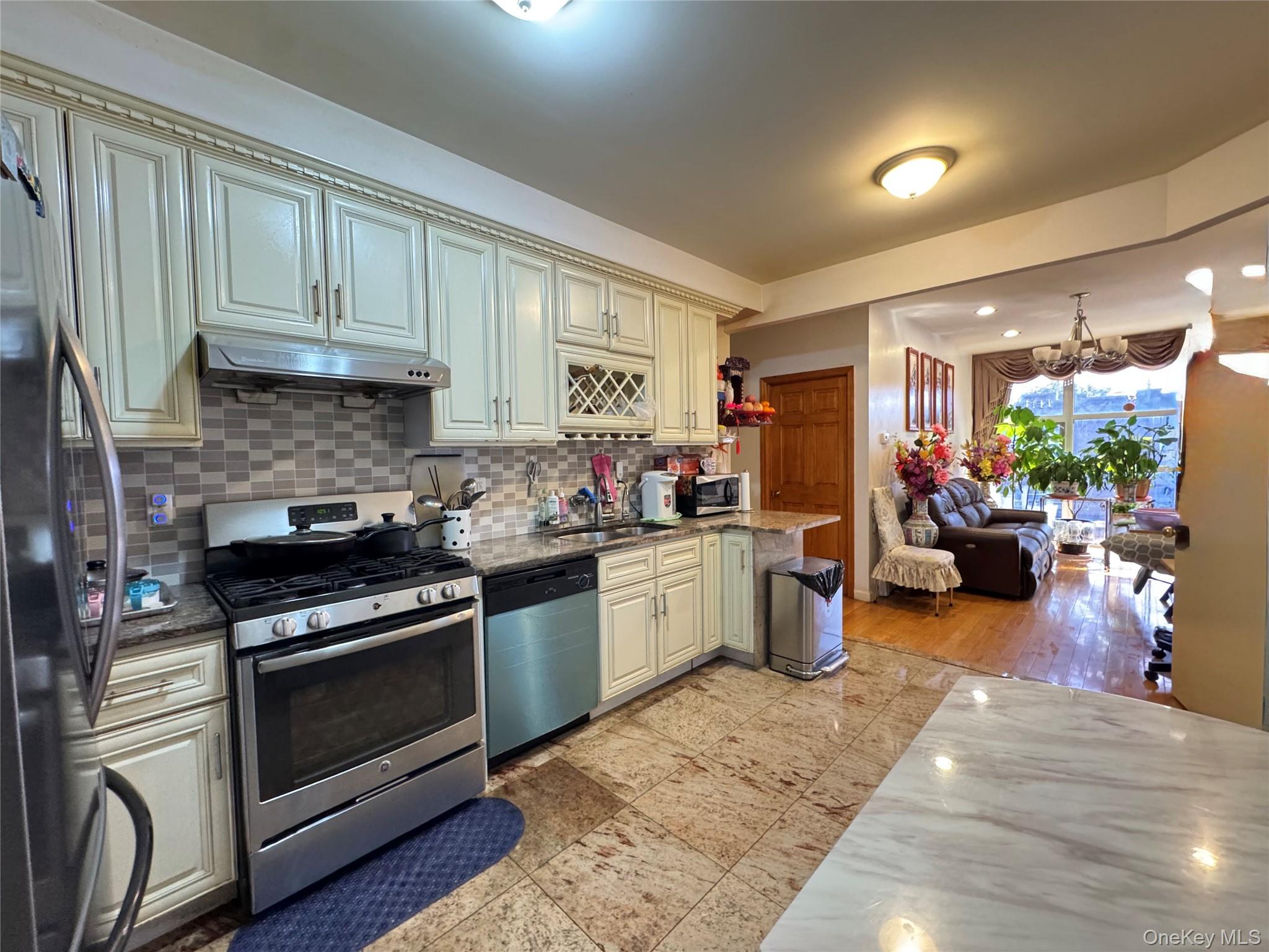42-16 162nd Street Queens, NY 11358 - Photo 16 of 16 Kitchen featuring dark stone counters, stainless steel appliances, decorative backsplash, under cabinet range hood, and open floor plan
