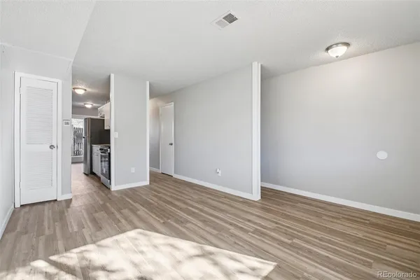a view of an empty room with wooden floor and a kitchen