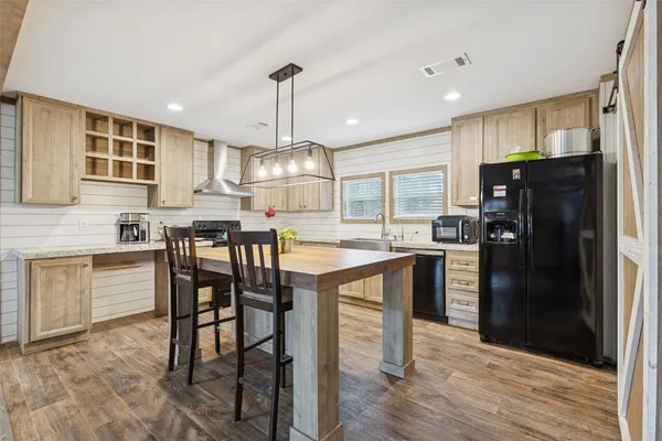 a kitchen with stainless steel appliances kitchen island granite countertop a refrigerator a stove a sink a dining table and chairs with wooden floor