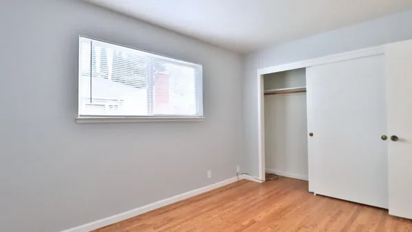 an empty room with wooden floor closet and windows