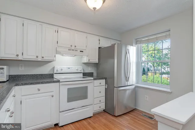 a kitchen with granite countertop white cabinets and white appliances with wooden floors