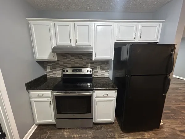 a kitchen with granite countertop white cabinets and refrigerator