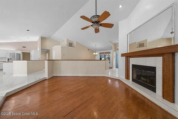 a view of a livingroom with a fireplace a ceiling fan and a kitchen view
