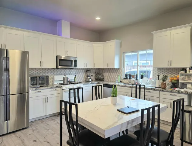 a kitchen with stainless steel appliances granite countertop a dining table chairs refrigerator and microwave