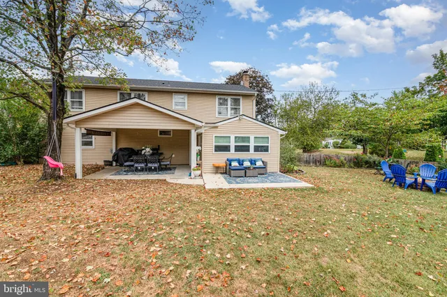 a view of a white house with large trees and lawn chairs