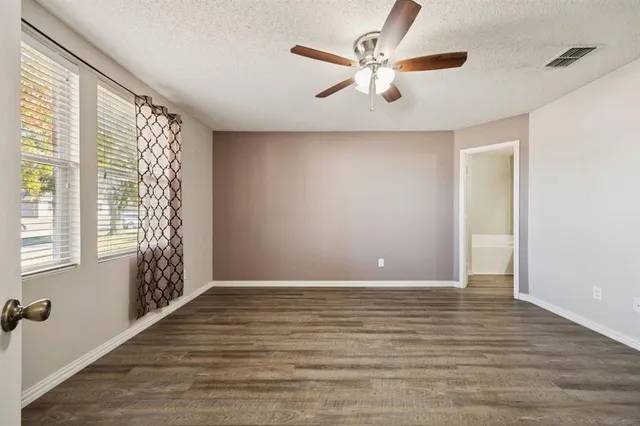 an empty room with wooden floor a ceiling fan and windows