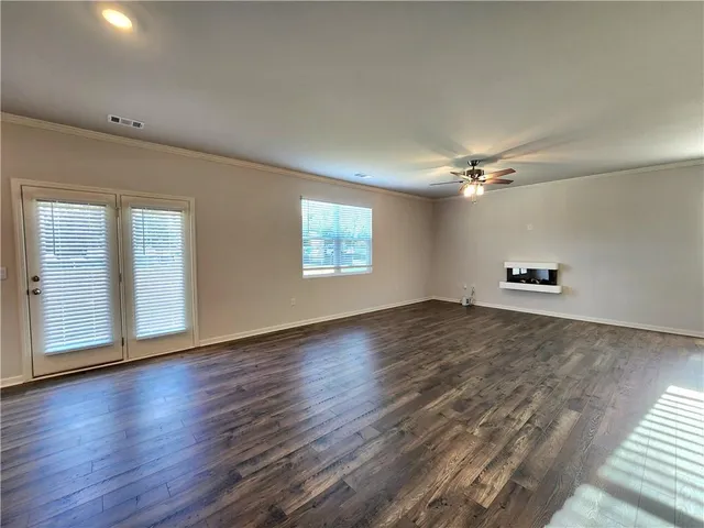 an empty room with wooden floor chandelier fan and windows
