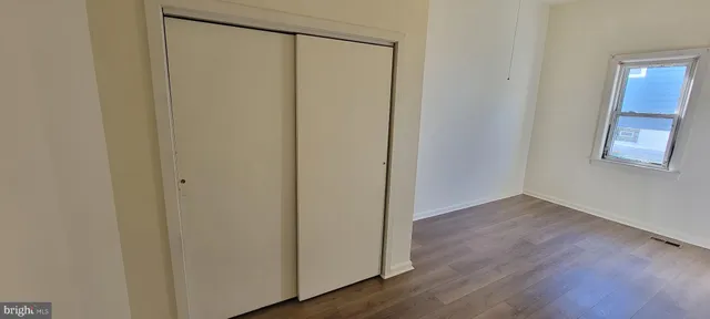 a view of an empty room with wooden floor and closet